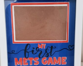 Puede incluir: Caja de sombra con marco blanco con fondo azul y área de fotos marrón. El texto "MY first METS GAME" se muestra en rojo y negro. La fecha "8-01-2025" está impresa en la parte inferior.