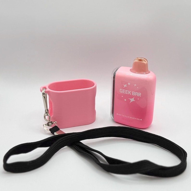 Op de afbeelding: Een roze Geek Bar wegwerp-vape-apparaat met een doorzichtig mondstuk en stermotieven, vergezeld van een bijpassende roze siliconen beschermhoes met een zilveren metalen clip en een lang zwart stoffen koord om te dragen.