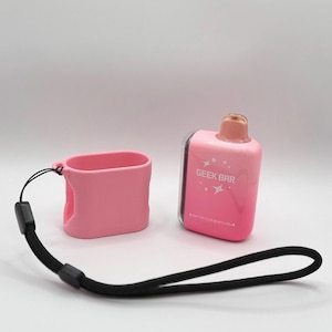 Op de afbeelding: Een roze Geek Bar wegwerp-vape-apparaat met een bijpassende roze siliconen beschermhoes en een zwart koord. Het apparaat heeft een roze verloopafwerking, een doorschijnend mondstuk en de tekst GEEK BAR op de voorzijde gedrukt.