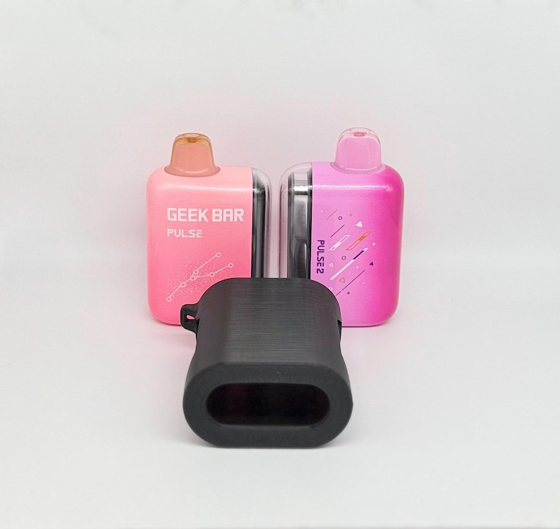 Op de afbeelding: Twee rechthoekige wegwerp-vape-apparaten, &eacute;&eacute;n lichtroze met het label GEEK BAR PULSE en &eacute;&eacute;n felroze met het label PULSE 2, geplaatst achter een zwarte siliconen beschermhoes met een hol midden en een getextureerd oppervlak.