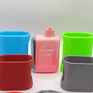 Op de afbeelding: Een roze Geek Bar wegwerp-vape met een perzikkleurig mondstuk, omringd door vier siliconen beschermhoezen in blauw, rood, limoengroen en grijs. Elke hoes is voorzien van een klein lusje voor bevestiging en een metalen sleutelhangerclip.