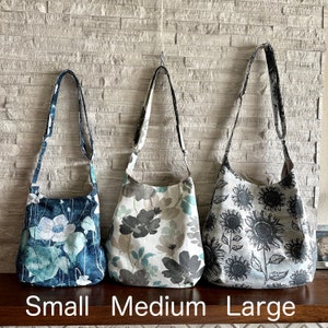 Puede incluir: Tres bolsos tote de estampado floral en diferentes tama&ntilde;os: peque&ntilde;o, mediano y grande. El bolso peque&ntilde;o es azul con flores blancas, el bolso mediano es blanco con flores grises y azules, y el bolso grande es gris con girasoles negros.