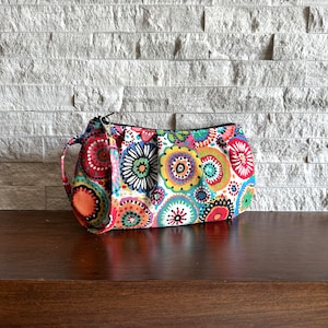 May include: A colorful, round-shaped pouch with a white background and a black zipper. The pouch is decorated with a pattern of colorful circles and dots.