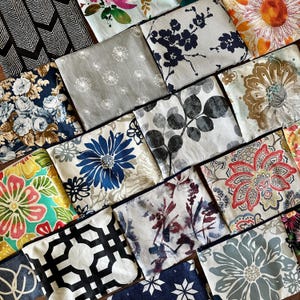 May include: A collection of square fabric pouches with various floral and geometric patterns. The pouches feature a range of colors, including blue, white, red, and black. Each pouch has a zipper closure.