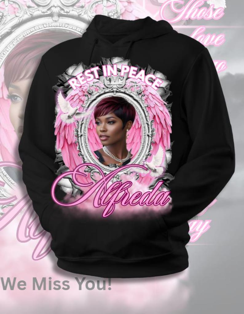 Pode incluir: Moletom preto com capuz com um retrato de uma mulher dentro de uma moldura com asas rosa, com as palavras "Rest in Peace" acima e "Alfreda" em it&aacute;lico abaixo. A frase "We Miss You!" est&aacute; na parte inferior.