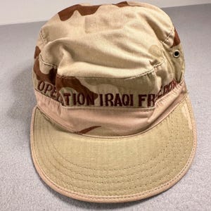 Peut inclure: Une casquette de patrouille camouflage beige et marron avec le texte brodé OPERATION IRAQI FREEDOM en lettres rouge foncé sur le panneau avant. La casquette présente un dessus plat, une visière rigide avec surpiqûres et un œillet métallique.