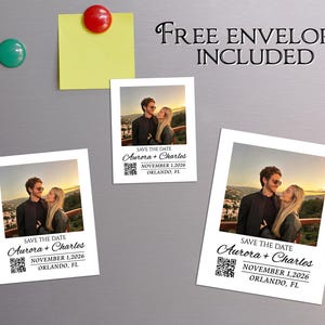 Könnte beinhalten: Drei weiße Save-the-Date-Karten mit einem Foto eines Paares, dem Text "Aurora + Charles" und dem Datum 1. November 2026. Die Karten liegen auf einer grauen Oberfläche mit einem gelben Haftzettel und Magneten. Der Text "Kostenlose Umschläge inklusive" ist ebenfalls sichtbar.