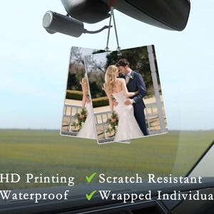 May include: Two square car air fresheners hanging from a rearview mirror. Each freshener displays a wedding photo of a couple embracing. The fresheners are labeled with the following features: HD Printing, Scratch Resistant, Waterproof, and Wrapped Individually.