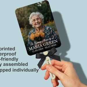 Puede incluir: Un abanico conmemorativo con una fotograf&iacute;a de una mujer sonriente sosteniendo flores. El abanico incluye el texto "In Loving Memory of MARIA GREEN 11.02.1954 - 05.27.2024" y est&aacute; adornado con una cinta negra. El abanico est&aacute; impreso en HD y es resistente al agua.