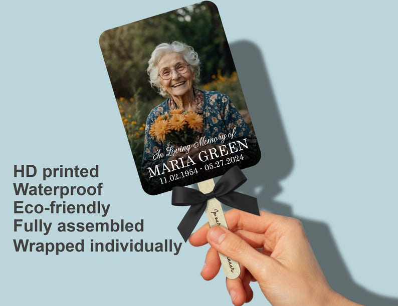 Puede incluir: Un abanico conmemorativo con una fotograf&iacute;a de una mujer sonriente sosteniendo flores. El abanico incluye el texto "In Loving Memory of MARIA GREEN 11.02.1954 - 05.27.2024" y est&aacute; adornado con una cinta negra. El abanico est&aacute; impreso en HD y es resistente al agua.