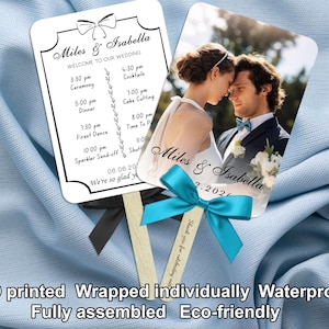 May include: Two wedding fans with wooden handles. One fan displays a wedding schedule with the names "Miles & Isabella." The other fan features a photo of the couple. Both fans have decorative bows and ribbons.