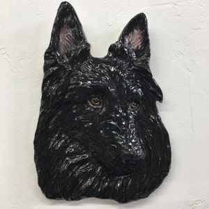 May include: A black ceramic sculpture of a dog's head. The dog has a glossy finish and realistic details, including brown eyes and a wet nose.