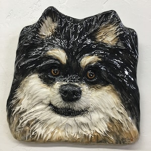 Può includere: Una scultura in ceramica di un viso di cane bianco e nero. Il cane ha il naso nero e gli occhi marroni. La scultura è dettagliata con la pelliccia e ha un aspetto realistico.