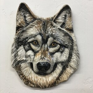 May include: A ceramic wolf sculpture with a detailed, realistic design. The wolf's fur is depicted in shades of brown, gray, and white, and its eyes are a piercing blue. The sculpture is a great addition to any home decor.