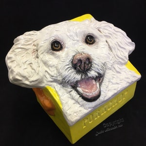 Op de afbeelding: Een wit keramisch beeld van een hondenkop met een gele doos waarop het woord "PORCUPINE" staat. De hond heeft een witte, pluche vacht en glimlacht met zijn mond open.