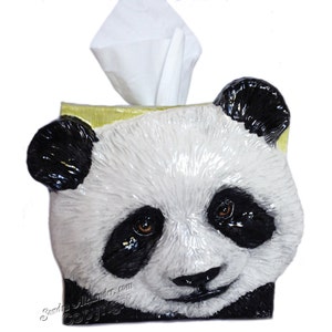 May include: A panda bear-shaped tissue box. The box is predominantly white with black detailing around the eyes, ears, and nose. White tissues protrude from the top. The panda's face features brown eyes and a smiling expression.