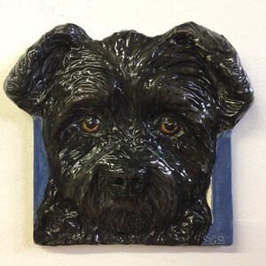 May include: A black ceramic sculpture of a dog's face, with a blue background and the signature "SFO" in the bottom right corner.