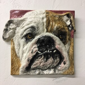 Può includere: Una scultura in ceramica del viso di un bulldog. La scultura è dipinta in tonalità di bianco, marrone e nero, e ha una texture realistica. Gli occhi del bulldog sono aperti e la sua bocca è leggermente aperta, mostrando i suoi denti.