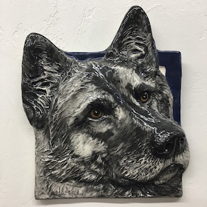 Può includere: Una scultura da parete in ceramica di una testa di cane, con un motivo di pelliccia bianco e nero, su sfondo blu.