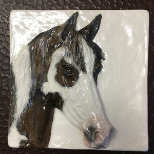 Könnte beinhalten: Eine weiße und braune Keramikfliese mit einer 3D-Reliefskulptur eines Pferdekopfes. Das Pferd hat ein weißes Gesicht mit braunen Markierungen und eine braune Mähne.
