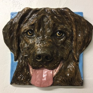 Può includere: Primo piano di una scultura di cane in ceramica marrone con la lingua rosa che sporge. La scultura è su uno sfondo blu.