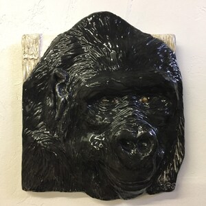 May include: A black ceramic sculpture of a gorilla's face. The sculpture is detailed with realistic features, including fur, eyes, and a nose.