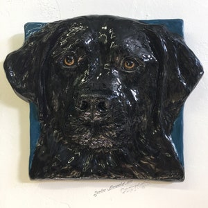 Può includere: Una scultura di testa di cane Labrador Retriever nero, con una finitura lucida, su sfondo blu turchese. La scultura è in ceramica e ha un aspetto realistico.