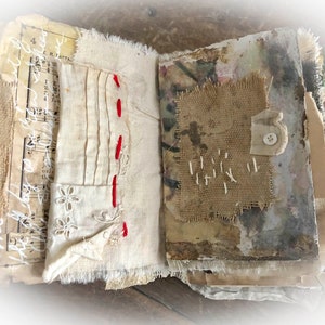 May include: An open journal with pages made of various fabrics, including burlap, lace, and linen. The pages are decorated with stitching, a button, and handwritten music notes.