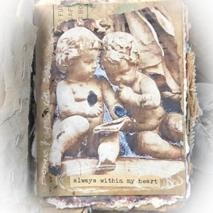 May include: A vintage-style collage featuring two cherub figurines with a faded background. The collage is decorated with textured paper and fabric. The text "always within my heart" is printed on a small piece of paper.