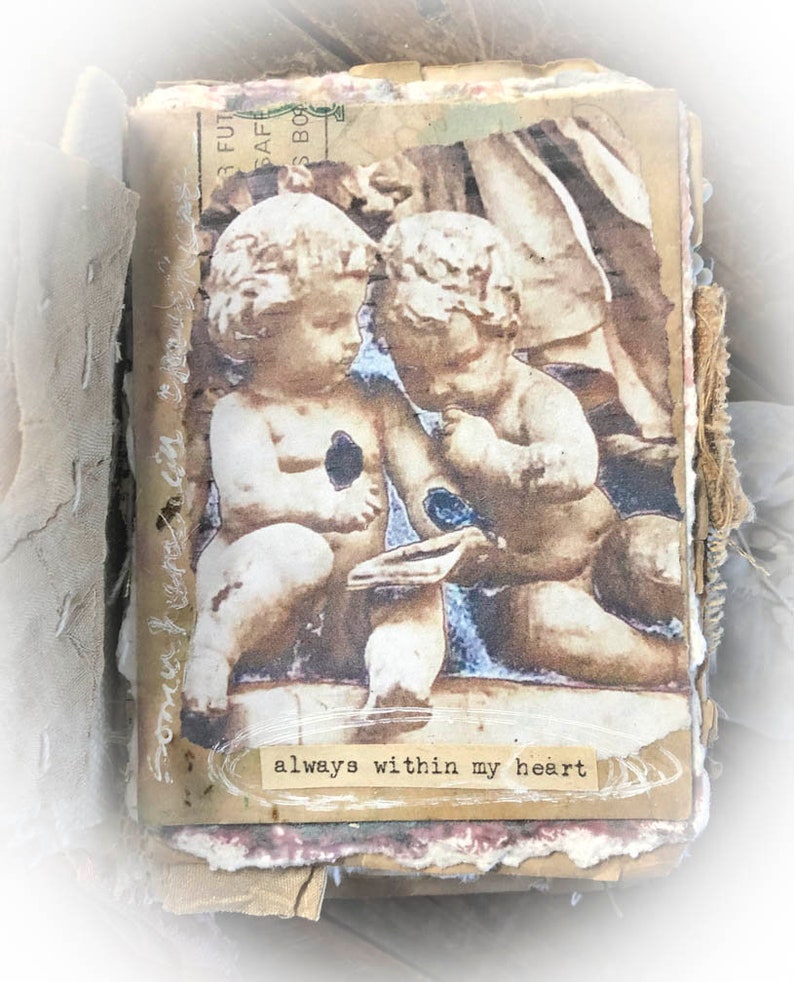 May include: A vintage-style collage featuring two cherub figurines with a faded background. The collage is decorated with textured paper and fabric. The text "always within my heart" is printed on a small piece of paper.