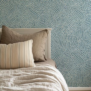 May include: Wallpaper featuring a teal blue background with a repeating pattern of small, white, teardrop-shaped marks arranged in swirling, organic lines. The design covers the wall behind a bed with a white headboard and neutral bedding.
