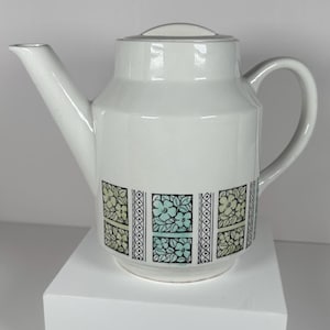 May include: White ceramic teapot with a geometric floral design in shades of green, yellow, and black.