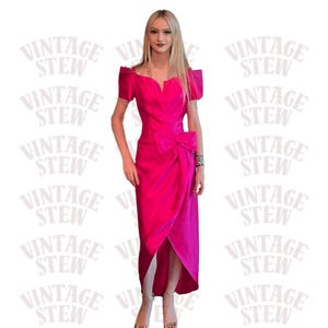 May include: A vibrant hot pink midi dress featuring short sleeves, a notched neckline, and a prominent bow detail at the waist. The skirt has a wrap-style front with a high-low hemline, creating a structured silhouette with a smooth, satin-like finish.