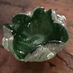May include: A decorative glass bowl with a ruffled edge. The bowl features a clear exterior and a vibrant green interior, creating a striking contrast. The bowl is designed with a unique, organic shape.