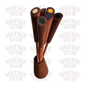 May include: A set of vintage wooden cocktail picks with colored tops, including white, yellow, blue, green, and black. The picks are displayed in a matching wooden holder. The background features the text "VINTAGE STEW".