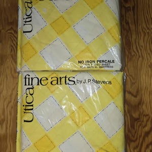 May include: Two twin fitted sheets in plastic packaging. The sheets have a yellow and white diamond pattern. The packaging reads "fine arts by J.P. Stevens" and "NO IRON PERCALE TWIN FITTED SHEET FOR 39x75 in. MATTRESS". The brand name "Utica" is also visible.
