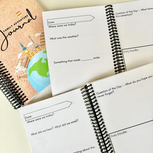May include: A spiral-bound "Family Adventure Journal" with a world map and travel landmarks on the cover. Open pages reveal prompts for daily entries, including questions about the day's events and space for doodles.