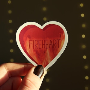 May include: A red heart-shaped sticker with a white outline and the word "FIREHEART" printed in white on the front.