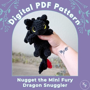 May include: A black crocheted dragon plush toy with large yellow eyes and a small red tail tip. The image includes the text Digital PDF Pattern and Nugget the Mini Fury Dragon Snuggler, presented against a purple background with white floral accents.