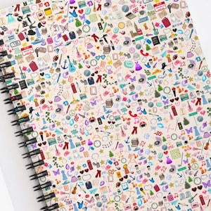 May include: Spiral-bound notebook with a cream-colored cover densely covered in colorful, tiny illustrations. The illustrations include clothing, musical notes, and other small objects. The notebook is open on a white surface, with a gold paper clip and sunglasses nearby.