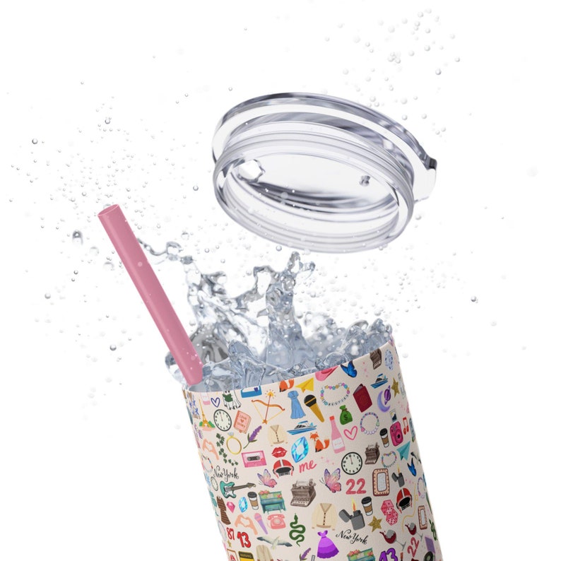 May include: A pink reusable straw sits in a white tumbler with a colorful pattern of various icons and text. The tumbler has a clear lid that is floating above the tumbler. Water is splashing around the tumbler.