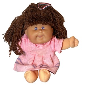 May include: A vintage doll with brown yarn hair and blue eyes. The doll wears a pink knit dress with purple stripes and has a ribbon in its hair. The doll's skin tone is tan, and it has a smiling expression.