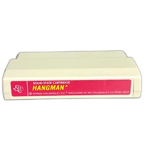 May include: A vintage Hangman solid state cartridge. The cartridge is off-white with a red label. The label features the game title in yellow and the text "SOLID STATE CARTRIDGE". The copyright information is also visible.