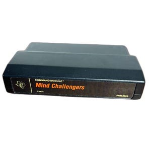 May include: Black Command Module video game cartridge labeled "Mind Challengers." The label is black with orange text and a logo. The cartridge is rectangular and has a stepped design.