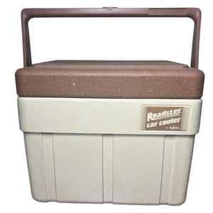 May include: A vintage Igloo Roadster car cooler in cream and brown. The cooler has a brown handle and lid, with the words "Roadster car cooler" printed on the front. The cooler is designed to keep items cold.