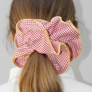 May include: Red and white gingham hair scrunchie with a yellow trim. The scrunchie is tied around a ponytail.