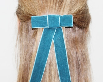 May include: A teal blue velvet bow hair clip. The bow is tied in a simple knot and has long tails.