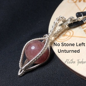 May include: A silver wire-wrapped pendant featuring a round, pink gemstone. The gemstone is encased in a woven wire design, suspended from a black cord. The text "No Stone Left Unturned" and the name "Aletha Tjaden" are visible.