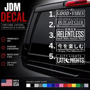 May include: A set of five white rectangular JDM decals featuring text and Japanese characters. The designs include Good Vibes, Outcast Club, Relentless Hard Work Forever Pays, Enjoy The Moment, and City Lights Late Nights, displayed on a dark vehicle window.