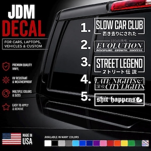 May include: A collection of five white vinyl decals displayed on a vehicle window. The designs feature text including SLOW CAR CLUB, EVOLUTION, STREET LEGEND, LATE NIGHTS CITY LIGHTS, and shit happens, with a colour palette selection bar at the bottom.